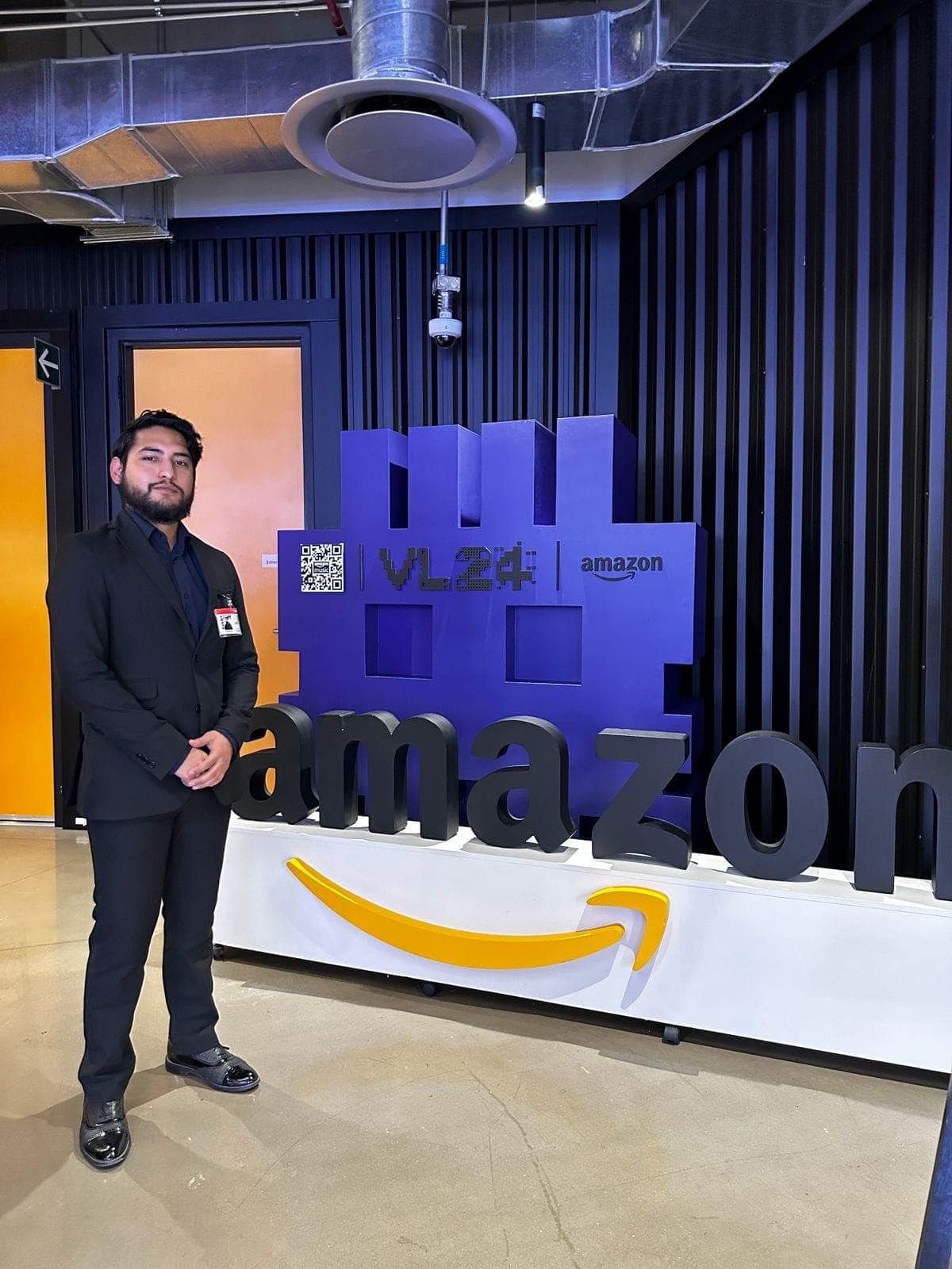 Ramses con traje frente al logo gigante de Amazon en el evento VL24.
