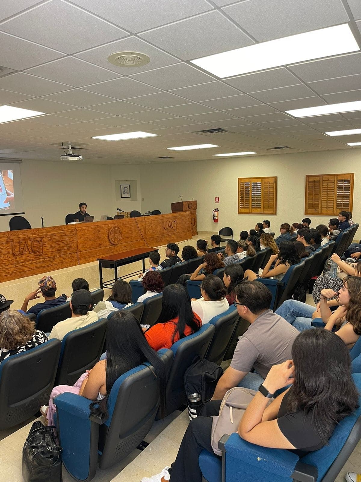 Auditorio lleno en la UACJ visto desde la parte trasera, con Ramses al frente.