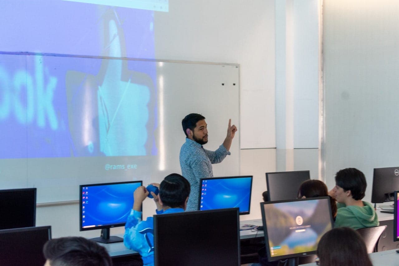Ramses dando clase frente a un grupo de estudiantes en un aula con computadoras.